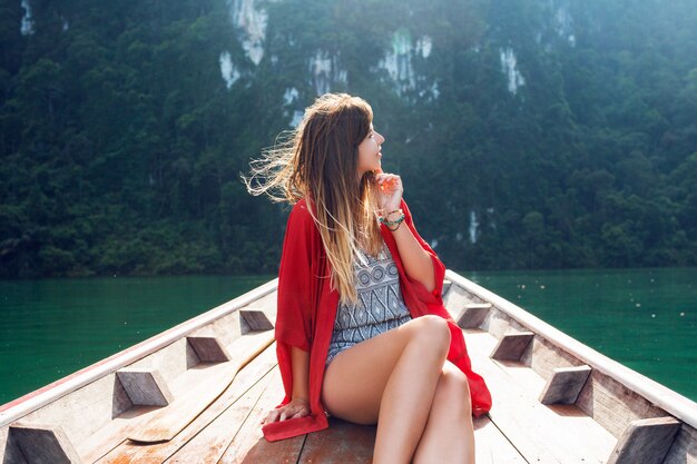 Lebensstilbild der hübschen Reisefrau, die im hölzernen langen Schwanzboot sitzt und auf wilde Natur und Berge schaut. Entdecken und Urlaubskonzept. Khao Sok See, Thailand.