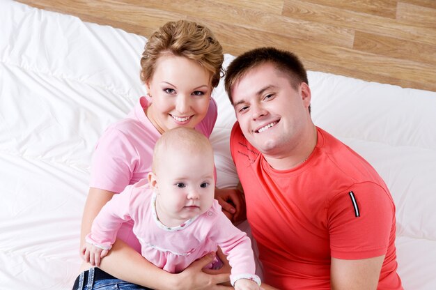 Lebensstilporträt der schönen jungen glücklichen Familie, die zu Hause im Bett liegt - hoher Winkel