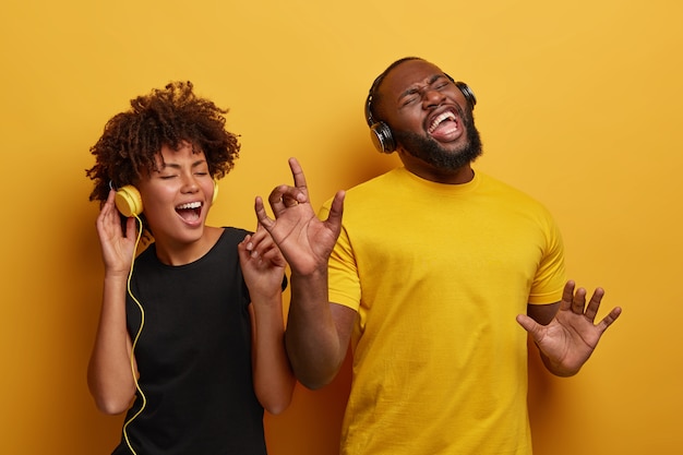 Lebhafte, energiegeladene, dunkelhäutige Paare tanzen und haben gemeinsam Spaß. Hören Sie verschiedene Arten von Musik in Kopfhörern, die auf hellem Hintergrund isoliert sind.