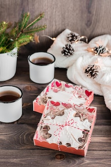 Lebkuchen mit schneeflockenförmigem zuckerguss in kisten und zwei tassen tee auf einem holztisch. weihnachtsgeschenk. vertikale ansicht
