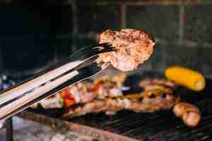 Kostenloses Foto lecker gegrilltes stück fleisch in einer metallzange