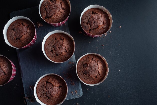 Leckere appetitliche Schokoladenmuffins in Tassen auf dunklem Hintergrund.