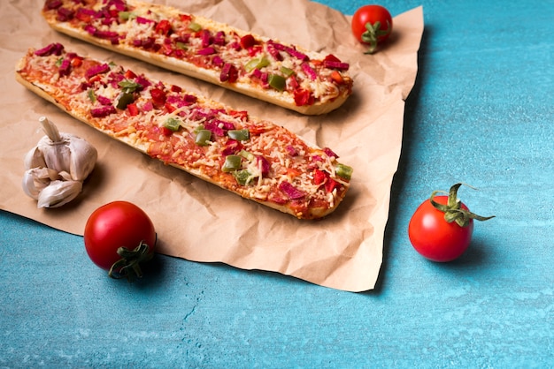 Leckere baguette-pizza; kirschtomate und -knoblauch auf braunem papier über blauem konkretem hintergrund