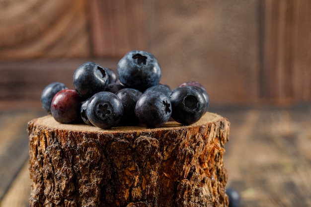 Leckere Blaubeeren in einem Holzstück auf Holz- und Steinfliesenhintergrund. Seitenansicht.