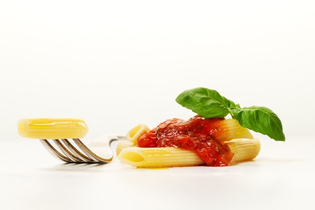 Leckere bunte appetitlich gekochte Spaghetti italienische Pasta mit Tomatensauce Bolognese und frischem Basilikum auf Gabel. Kreative Portion, Nahaufnahme.