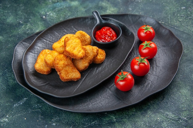 Kostenloses Foto leckere chicken nuggets und ketchup-tomaten in schwarzen tellern auf dunkler oberfläche mit freiem platz