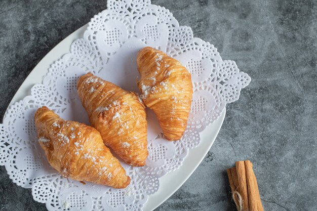 Leckere Croissants mit Zimtstangen auf Grau.