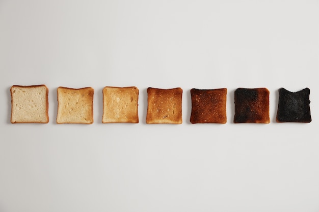 Leckere geröstete Brotscheiben von ungeröstet bis verbrannt. Stufen der Röstung. Selektiver Fokus. Knuspriger leckerer Snack. weiße Oberfläche. Satz Toast, jeder für längere Zeit geröstet, Röstgrad.