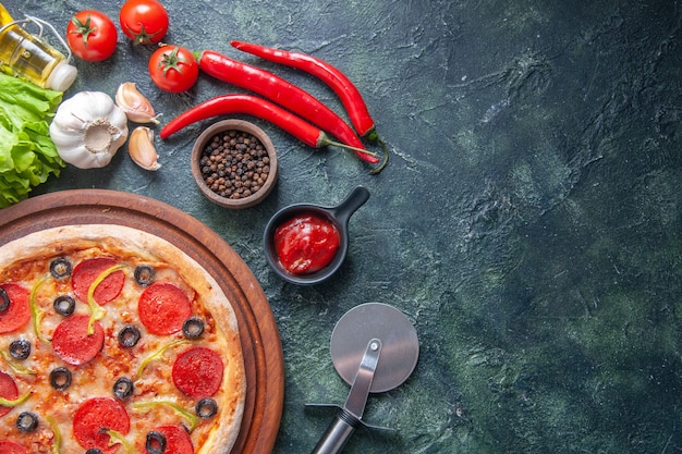 Leckere hausgemachte Pizza auf Holzbrett Tomaten Ketchup Knoblauch Pfeffer Öl Flasche grünes Bündel auf dunkler Oberfläche in Nahaufnahme