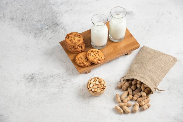 Leckere Kekse mit Bio-Erdnüssen und Glas Milch auf Holzbrett.
