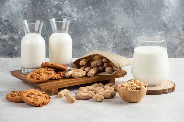 Leckere Kekse mit Bio-Erdnüssen und Honig mit Glas Milch auf Holzbrett.