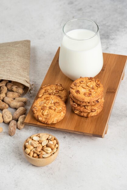 Leckere Kekse mit Honig und Erdnüssen und Glas Milch auf Holzbrett.