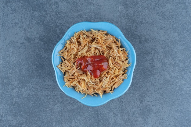 Leckere Makkaroni mit Ketchup in blauer Schüssel.