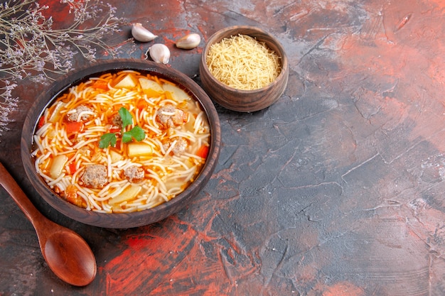 Leckere Nudelsuppe mit Hühnchen und ungekochten Nudeln in einer kleinen braunen Schüssel und Löffel auf dunklem Hintergrund