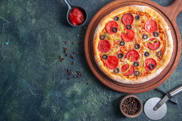 Leckere Pizza auf Holzbrett und Pfefferketchup auf isolierter dunkler Oberfläche in Nahaufnahme