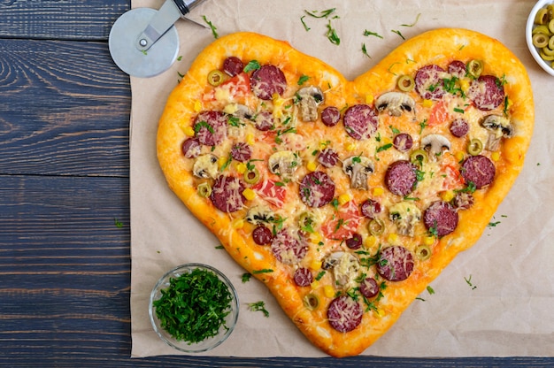 Leckere pizza in herzform mit pilzen, salami, peperoni, oliven, mais