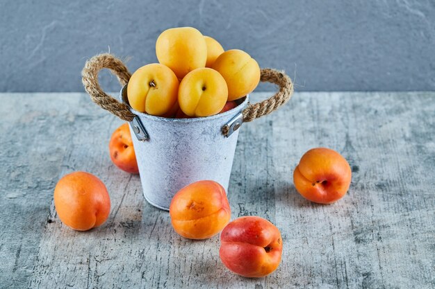 Leckere reife Aprikosen im Eiseneimer mit Nektarinen auf Marmoroberfläche