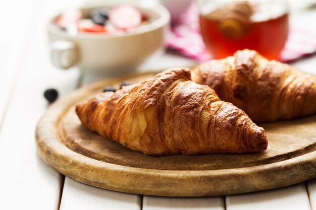 Leckere schöne Croissants auf Holzbrett. Traditionelles kontinentales Frühstück. Granola mit Früchten und Honig auf Hintergrund.