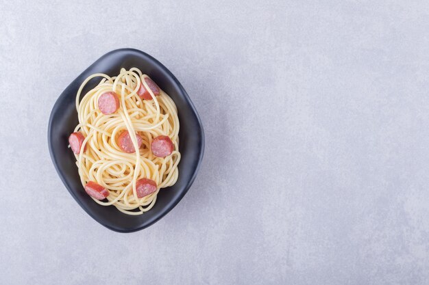 Leckere Spaghetti mit geschnittenen Würstchen in schwarzer Schüssel.