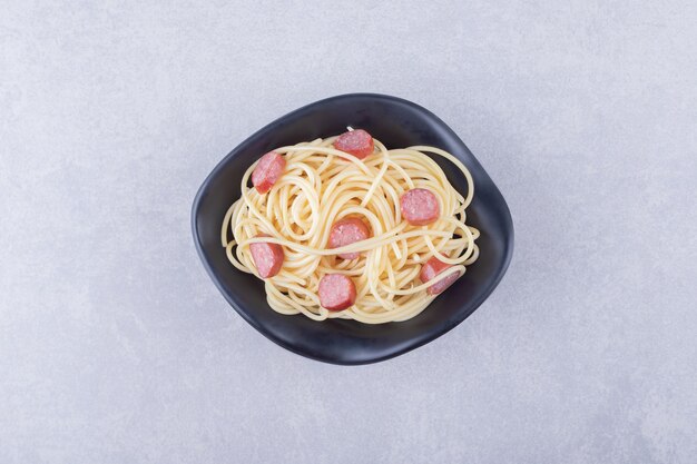 Leckere Spaghetti mit geschnittenen Würstchen in schwarzer Schüssel.