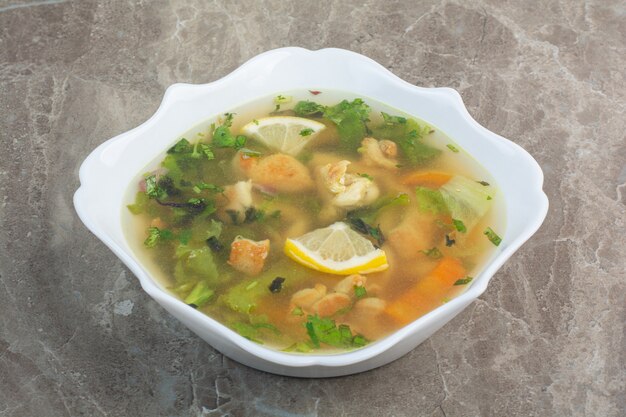 Leckere Suppe mit Gemüse und Zitronenscheiben auf weißem Teller.