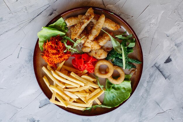 Leckere Vorspeisen im Restaurant für große Unternehmen, darunter goldene Hühnernuggets, Bratkartoffeln, grüne Salatblätter und frische Gurken, die auf einem weißen Tisch stehen und köstlich aussehen