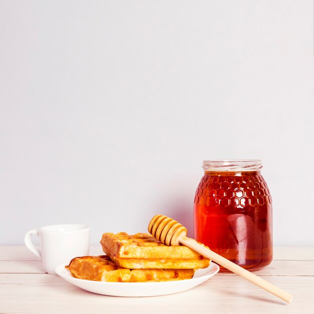 Leckere Waffel; Glas Honig und Kaffee zum Frühstück auf Holztisch