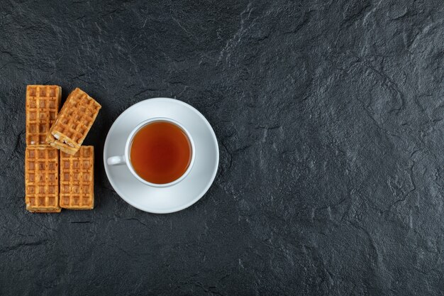 Leckere Waffeln mit einer Tasse Aromatee auf dunkler Oberfläche.