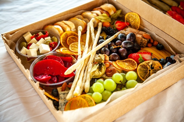Leckere weinsnacks im karton für ein partybuffet: käse, wurst, aufschnitt, obst, baguette, grissini