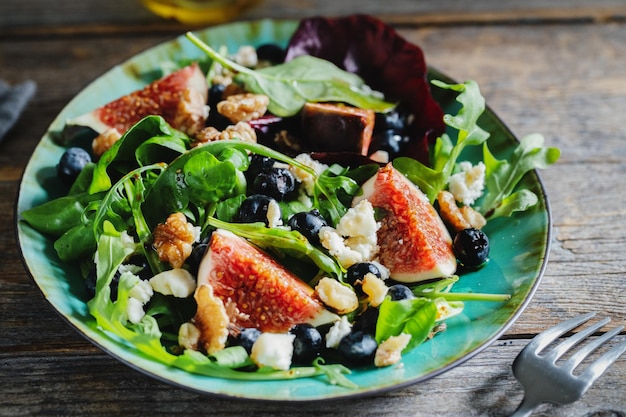 Leckerer, appetitlicher Herbstsalat mit Feigen-Blaubeeren-Käse-Nüssen und Rucola serviert auf Teller auf dunklem Hintergrund.