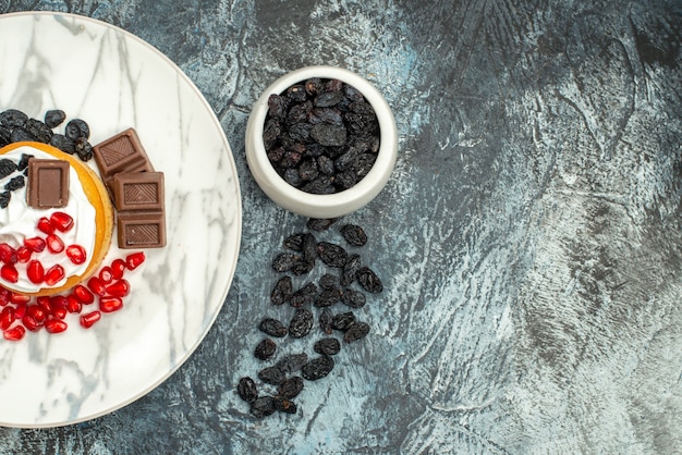 Leckerer cremiger Kuchen der Draufsicht mit Schokoladengranatäpfeln und Rosinen auf hellem dunklem Hintergrund