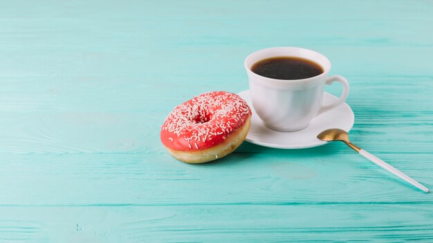 Leckerer Donut mit Tasse Tee und Löffel auf grüner Tabelle