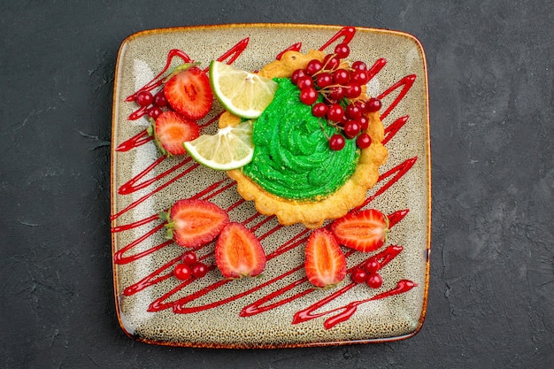 Leckerer Kuchen der Draufsicht mit grüner Sahne und Erdbeeren auf dem süßen Hintergrunddesserttee des dunklen Hintergrunds