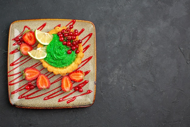 Leckerer kuchen der draufsicht mit grüner sahne und erdbeeren auf dem süßen hintergrunddesserttee des dunklen hintergrunds