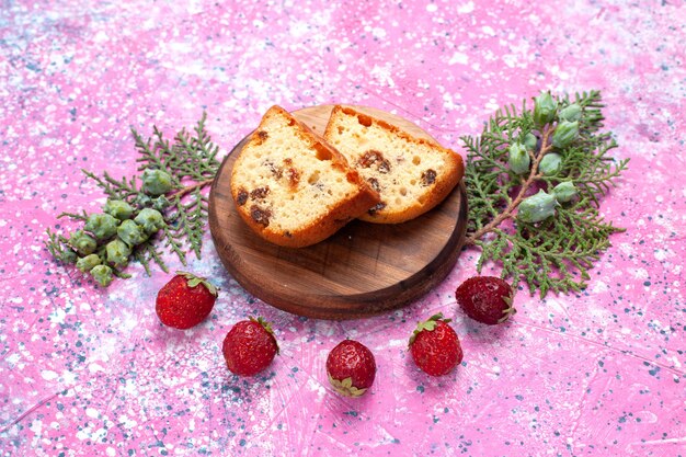 Leckerer Kuchen der halben Draufsicht süß und lecker geschnitten mit frischen roten Erdbeeren auf rosa Schreibtisch.