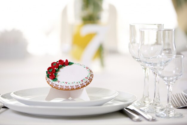 Leckerer Lebkuchen mit Glasur bedeckt und mit winzigen roten Rosen und Muster verziert steht auf dem festlichen Hochzeitstisch mit Gläsern und anderen Gerichten. Sieht lecker und süß aus.