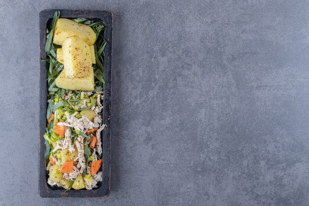 Leckerer Salat und Salzkartoffeln auf schwarzem Teller.