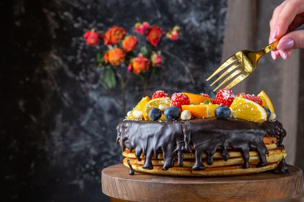 Leckerer Schokoladenkuchen der Vorderansicht mit frischen Früchten auf dunkler Wand