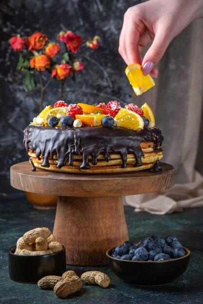 Leckerer Schokoladenkuchen der Vorderansicht mit frischen Früchten auf dunkler Wand