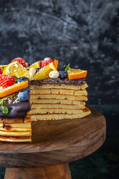 Leckerer Schokoladenkuchen der Vorderansicht mit Früchten auf dunkler Wand