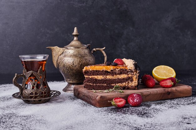 Leckerer Schokoladenkuchen mit Teeservice und Früchten auf dunklem Hintergrund.