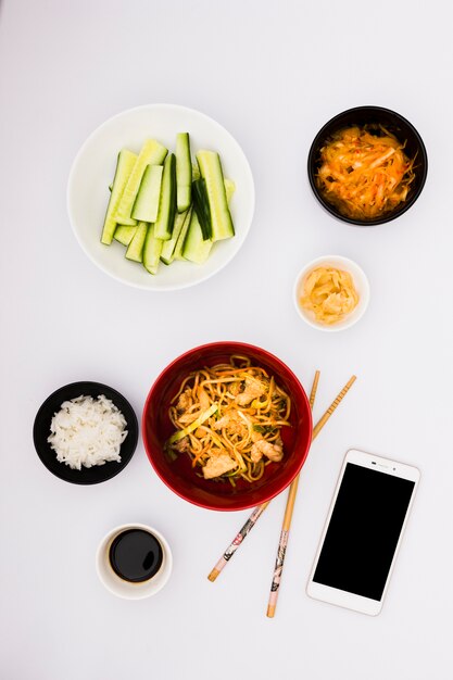 Leckeres asiatisches Essen mit Salat; Saucen und Smartphone auf weißem Hintergrund
