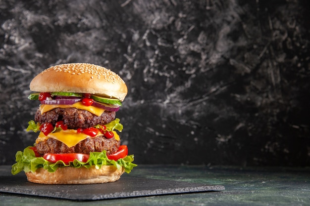 Leckeres Fleischsandwich mit Tomatengrün auf dunklem Farbtablett auf der rechten Seite auf schwarzer Oberfläche