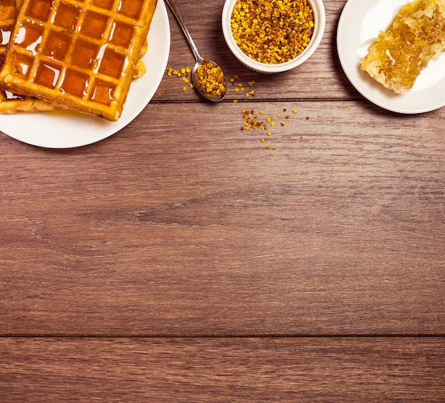 Leckeres frühstück mit waffel; süßer honig- und bienenpollen über hölzernem schreibtisch