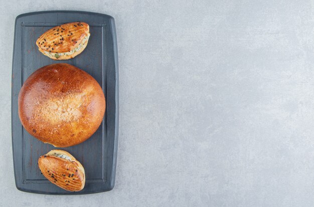 Leckeres Gebäck mit Käse und Brötchen auf schwarzem Brett.