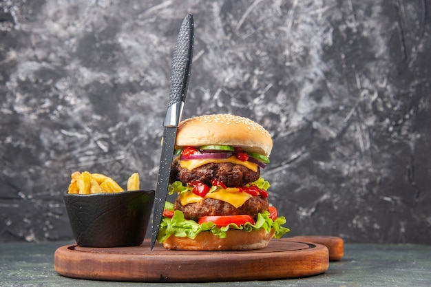 Leckeres hausgemachtes Sandwich-Tomaten-Pommes-Messer auf Holzschneidebrett auf dunkler Farboberfläche