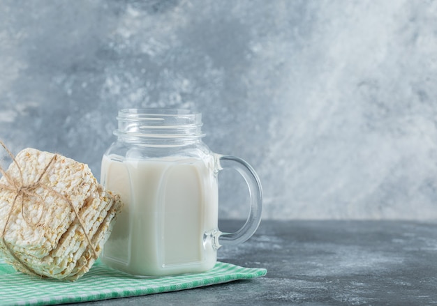 Leckeres quadratisches Knäckebrot und eine Flasche Milch auf Marmor.