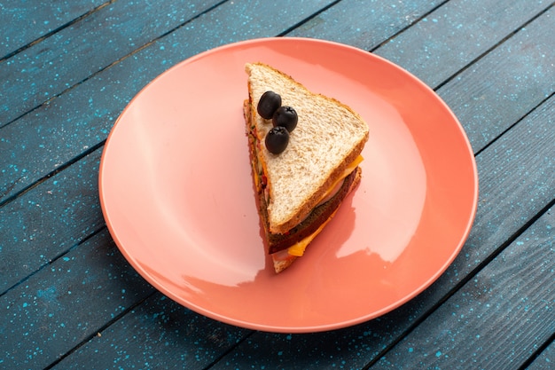 Leckeres Sandwich der Draufsicht mit Olivenschinkentomaten innerhalb der rosa Platte auf dem blauen hölzernen Hintergrundsandwich-Nahrungsmittelsnack-Mittagessen