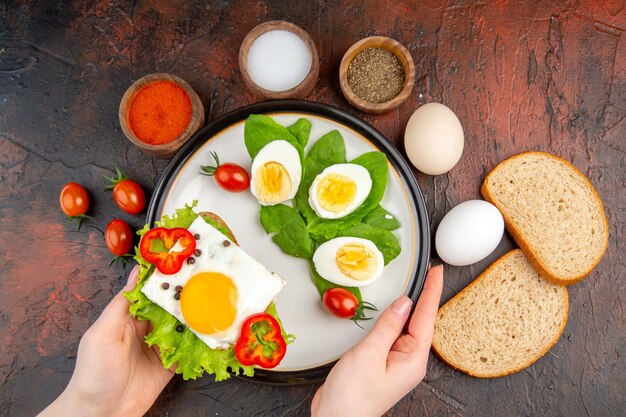 Leckeres Sandwich mit Eiergewürz und Tomaten auf dunklem Tisch von oben