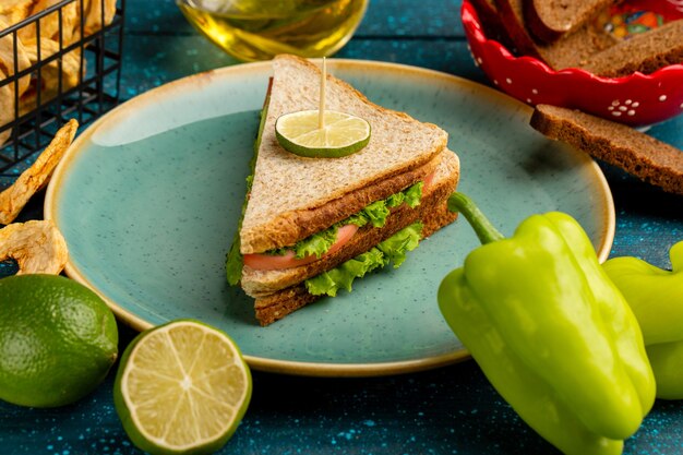 leckeres Sandwich mit grünem Salatschinken und Tomaten als Füllung zusammen mit Zitrone und Öl auf Blau